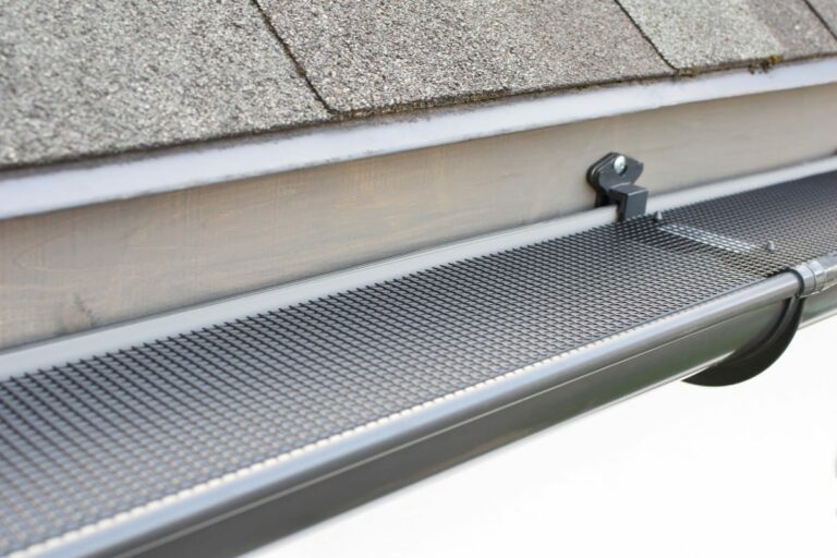 Plastic guard over new dark grey plastic rain gutter on asphalt shingles roof at shallow depth of field.